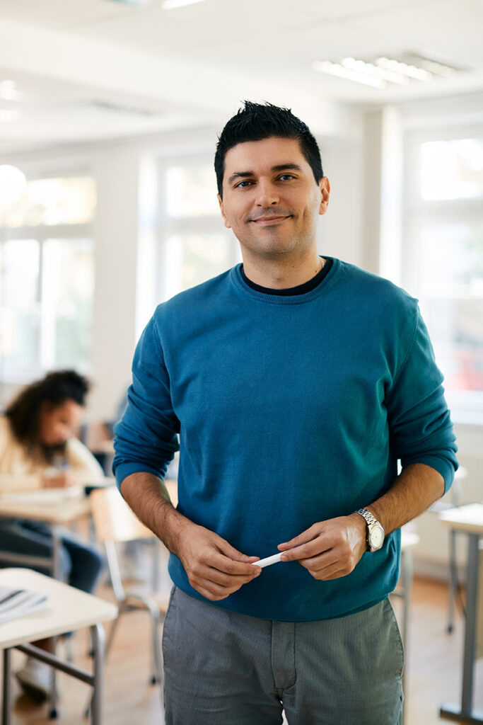 Portrait of high school teacher stands in classroom and looks at camera.