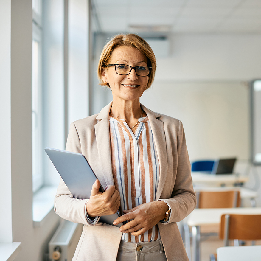 Portrait of smiling mature school administrator with laptop in the classroom.