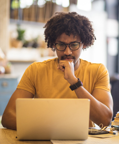 A twenty-something man in front of a laptop with a contemplative look